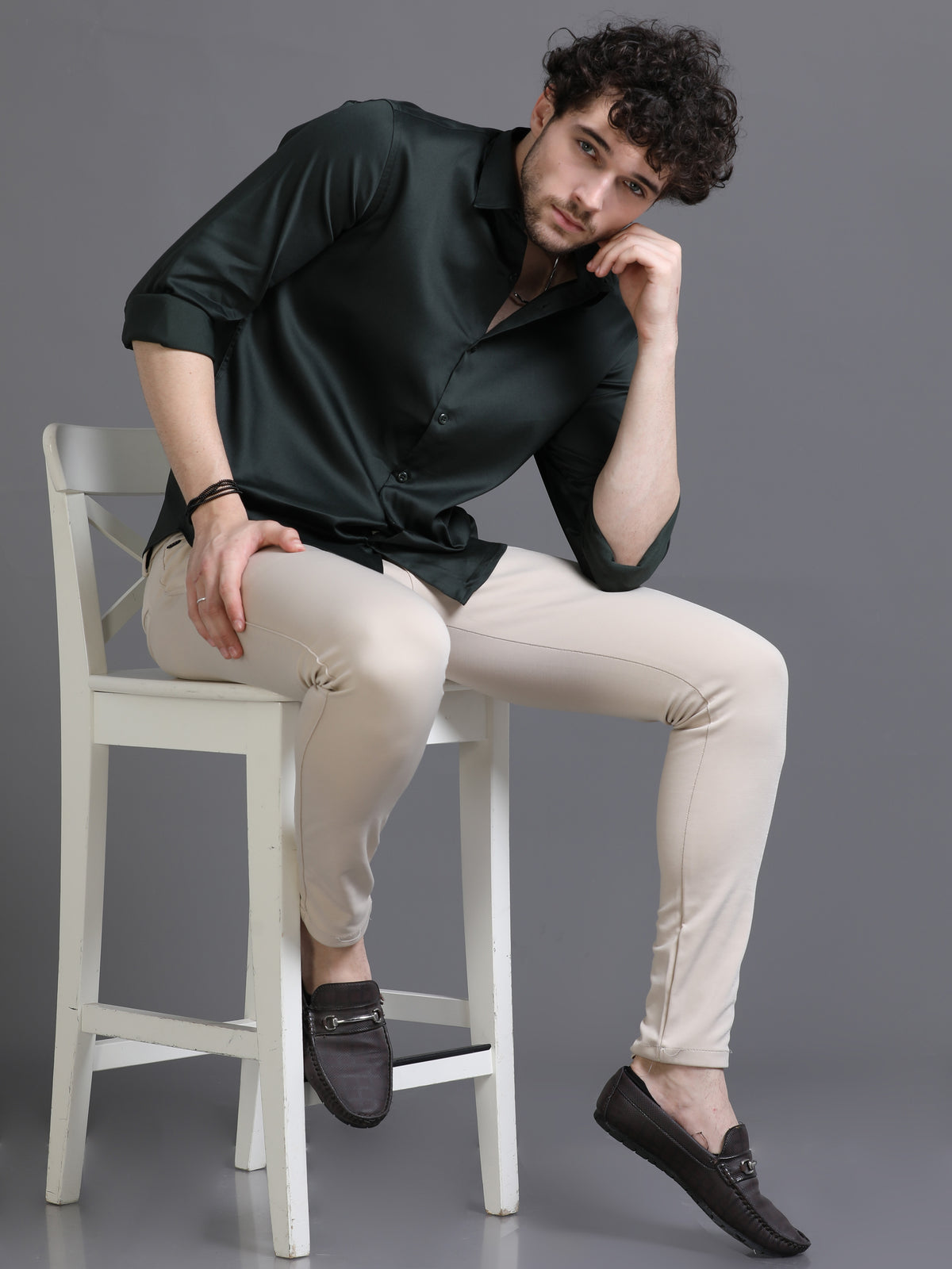 Formal plain green shirt for men worn by a seated model with beige trousers and loafers